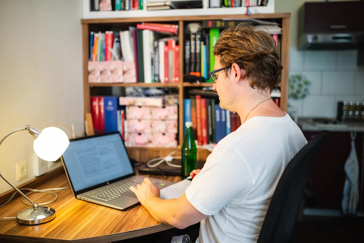 A student works on a laptop at a desk in front of a bookshelf