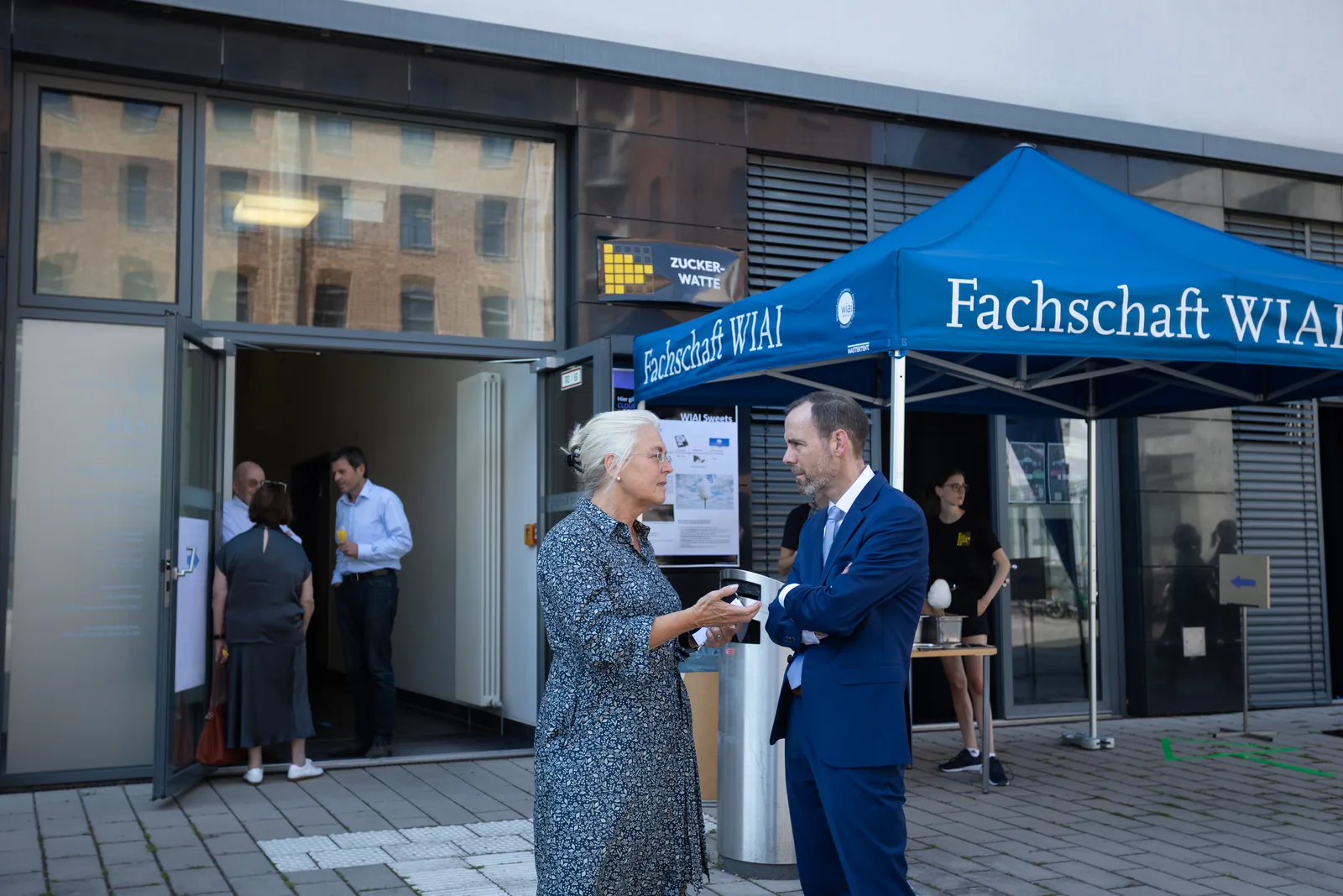 Two people talk in front of the student council&rsquo;s blue tent at the entrance of a faculty building