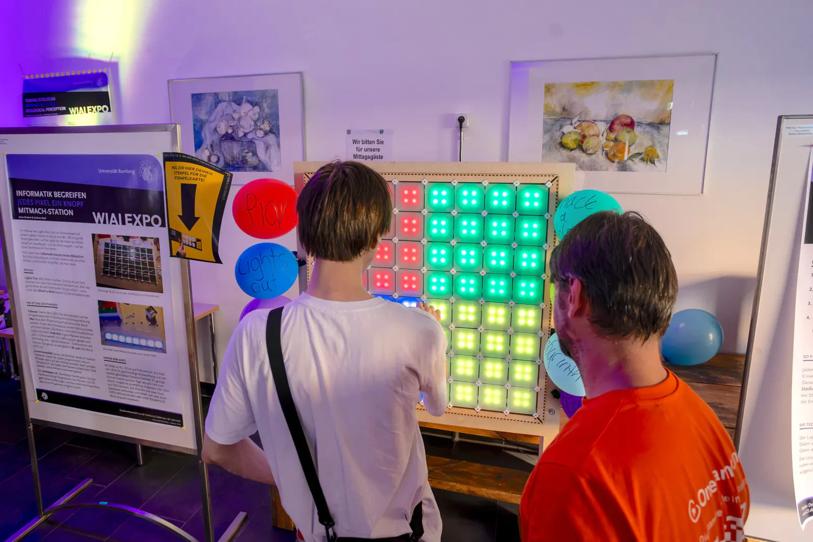 Two visitors press glowing buttons on a large LED game wall