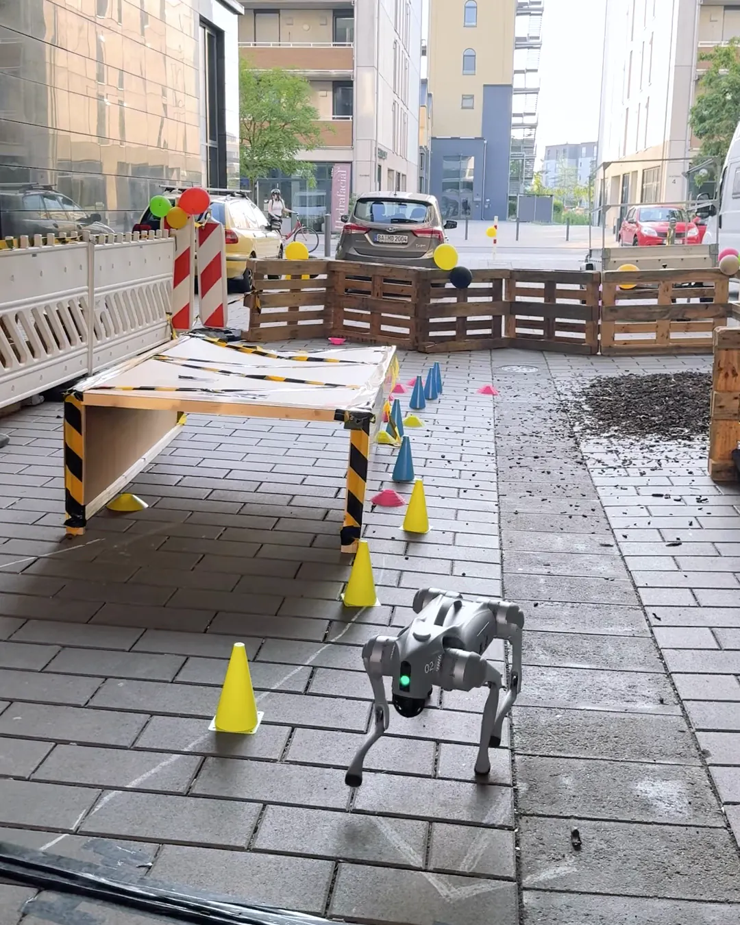 A four-legged robot dog walks through an obstacle course of traffic cones and wooden pallets